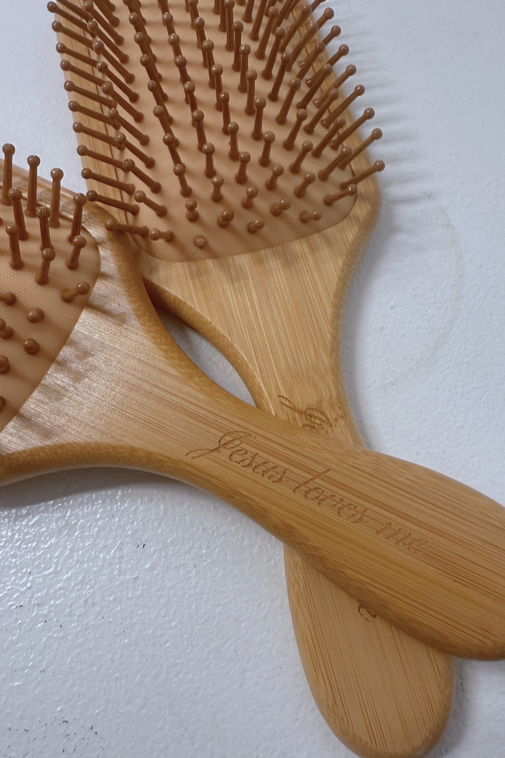 Two wooden hairbrushes held by a hand against a light gray background