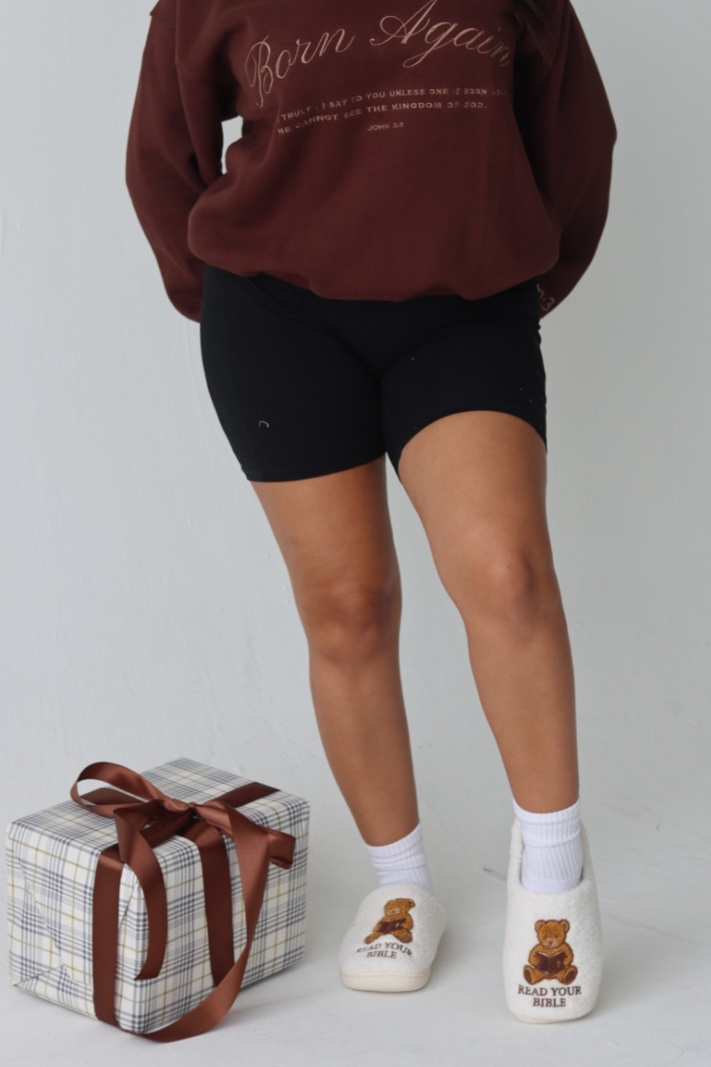 White slippers with teddy bear design and 'Read Your Bible' text on a plaid surface.