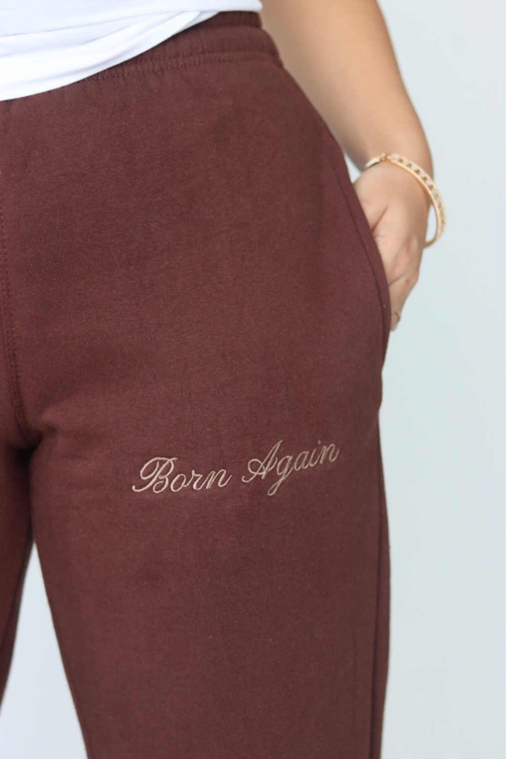 Woman wearing a white sleeveless top and brown pants against a plain background