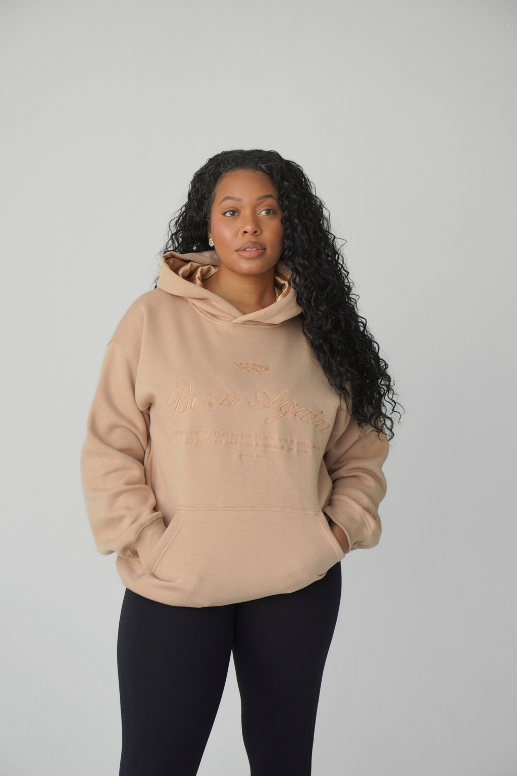 Woman wearing a beige hoodie with text on a plain background